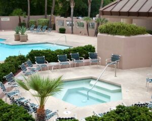 a concrete pool deck with lounge chairs and palm trees in the city.