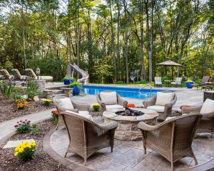 A city backyard with a fire pit and wicker furniture surrounded by concrete sidewalks.