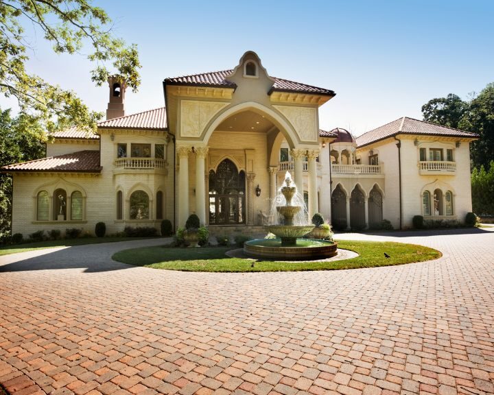 A mansion in the city, with an ornate design and a fountain on its concrete driveway.