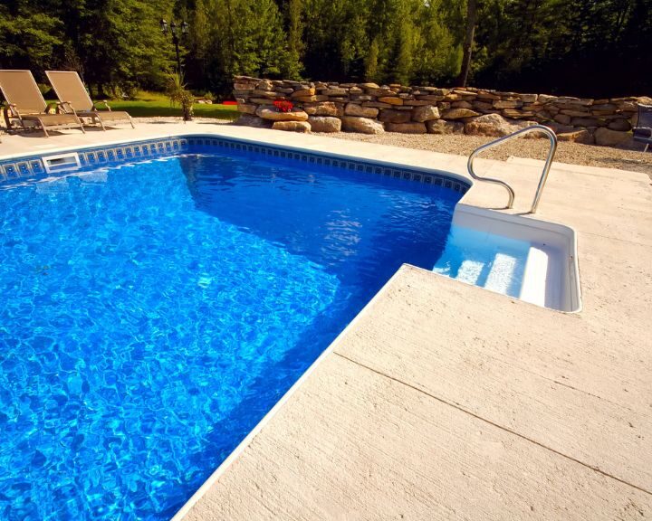 A concrete pool deck surrounds a blue liner swimming pool in the city backyard.