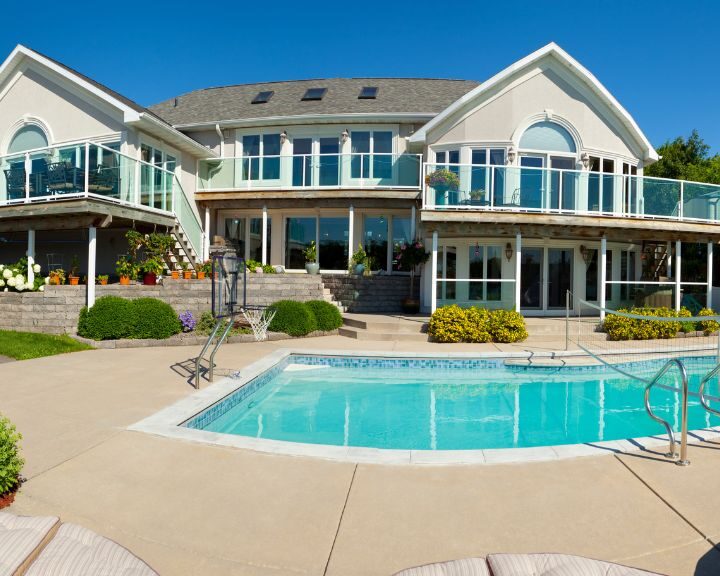 A large city house with a concrete pool deck and lounge chairs.